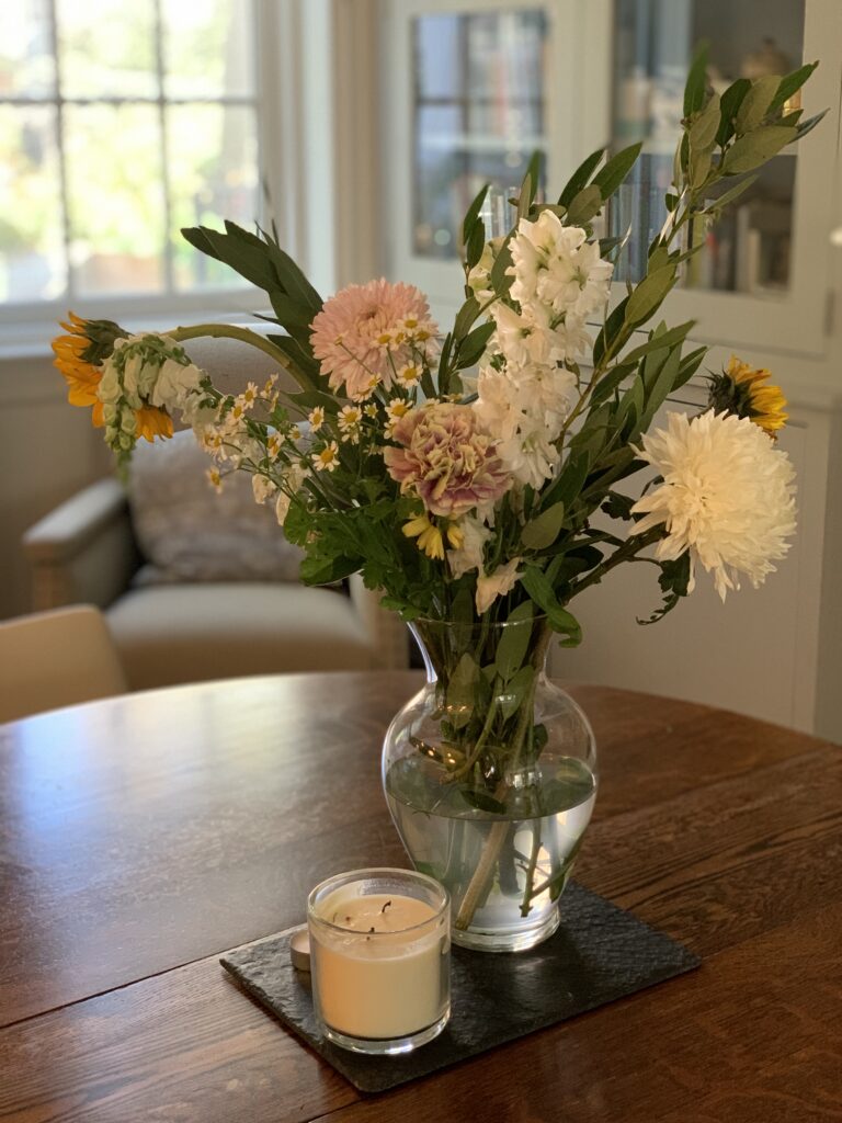 A vase of flowers on the table in front of a candle.