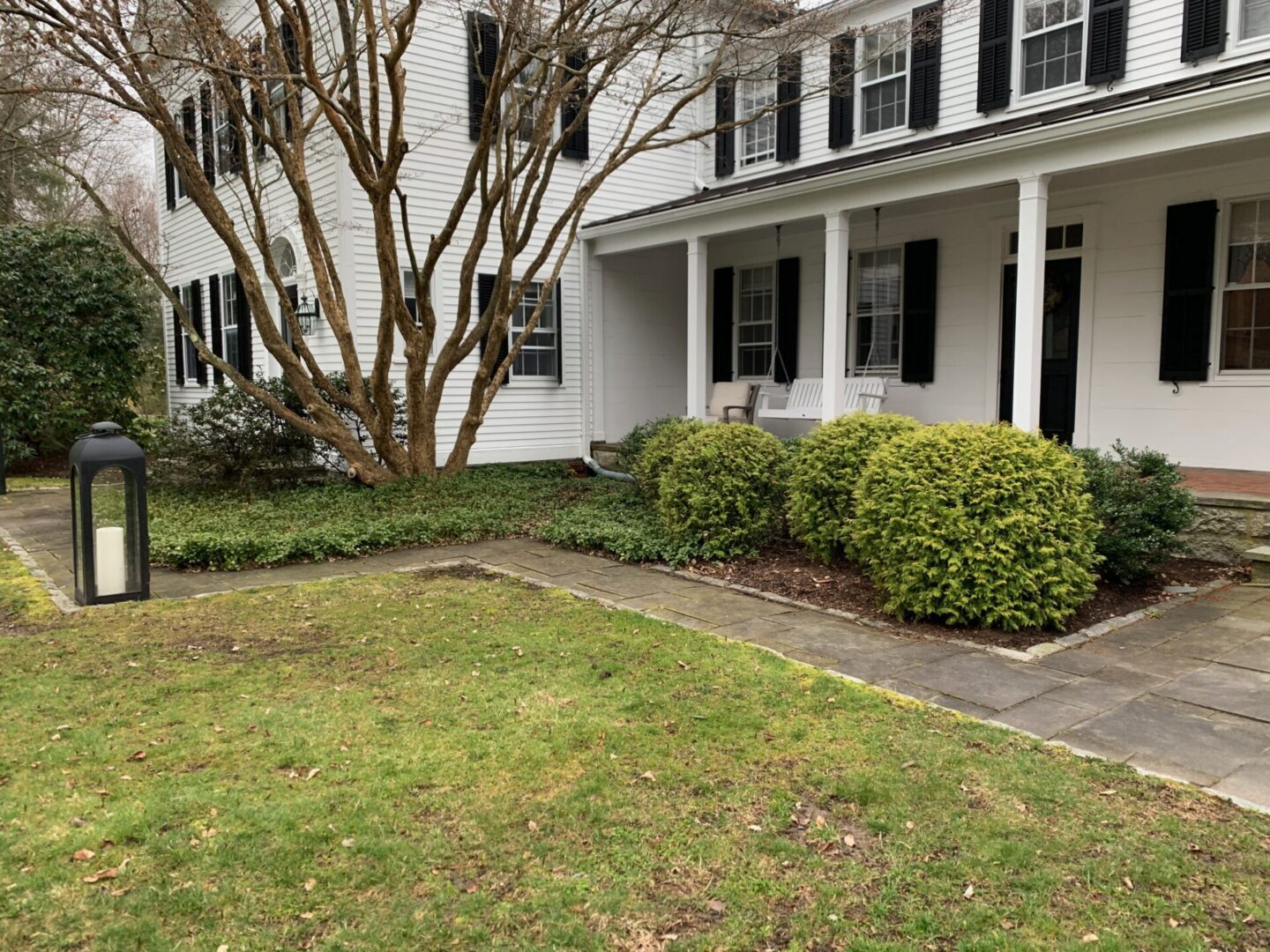 A white house with bushes and trees in front of it.