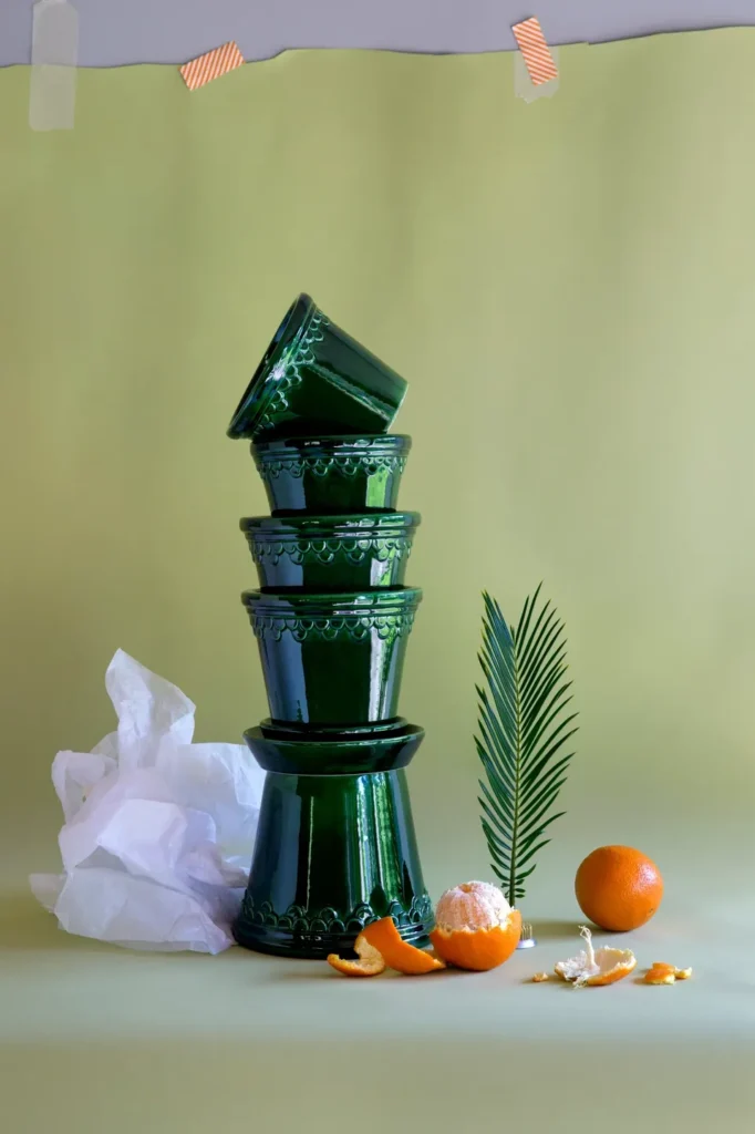 A stack of green glass bowls next to an orange and some leaves.