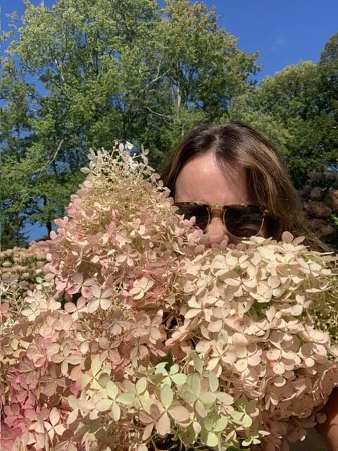 Person with sunglasses holding large hydrangea flowers.